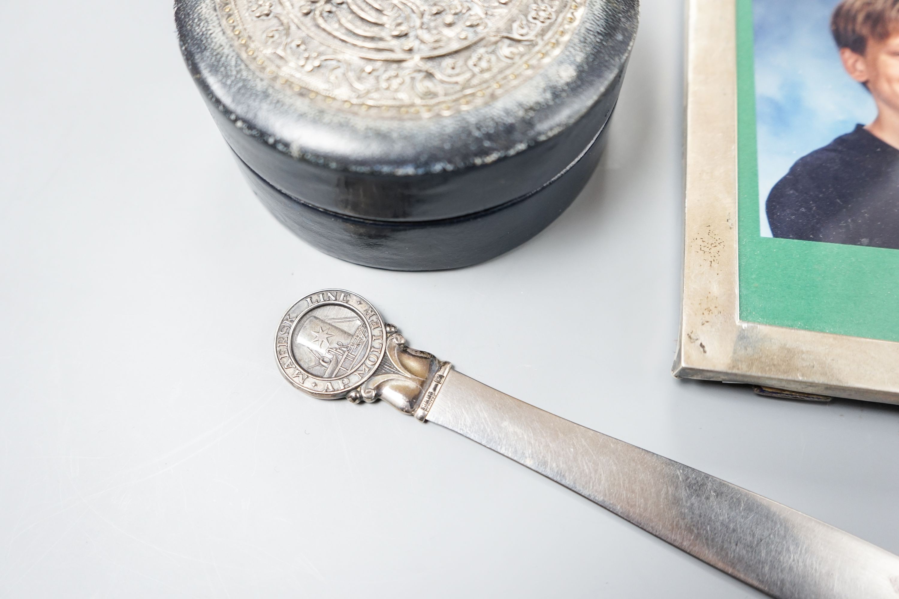 An Edwardian silver mounted photograph frame, 15.5cm, a letter opener with white metal finial and blue leather stud box with Far Eastern embossed white metal panel to lid.